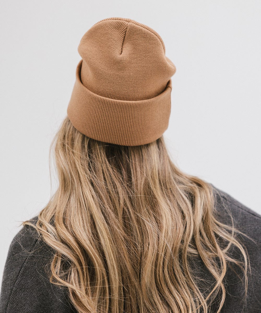 Woman wearing a latte colored knit beanie and a grey sweater, facing behind against a plain background #color_latte
