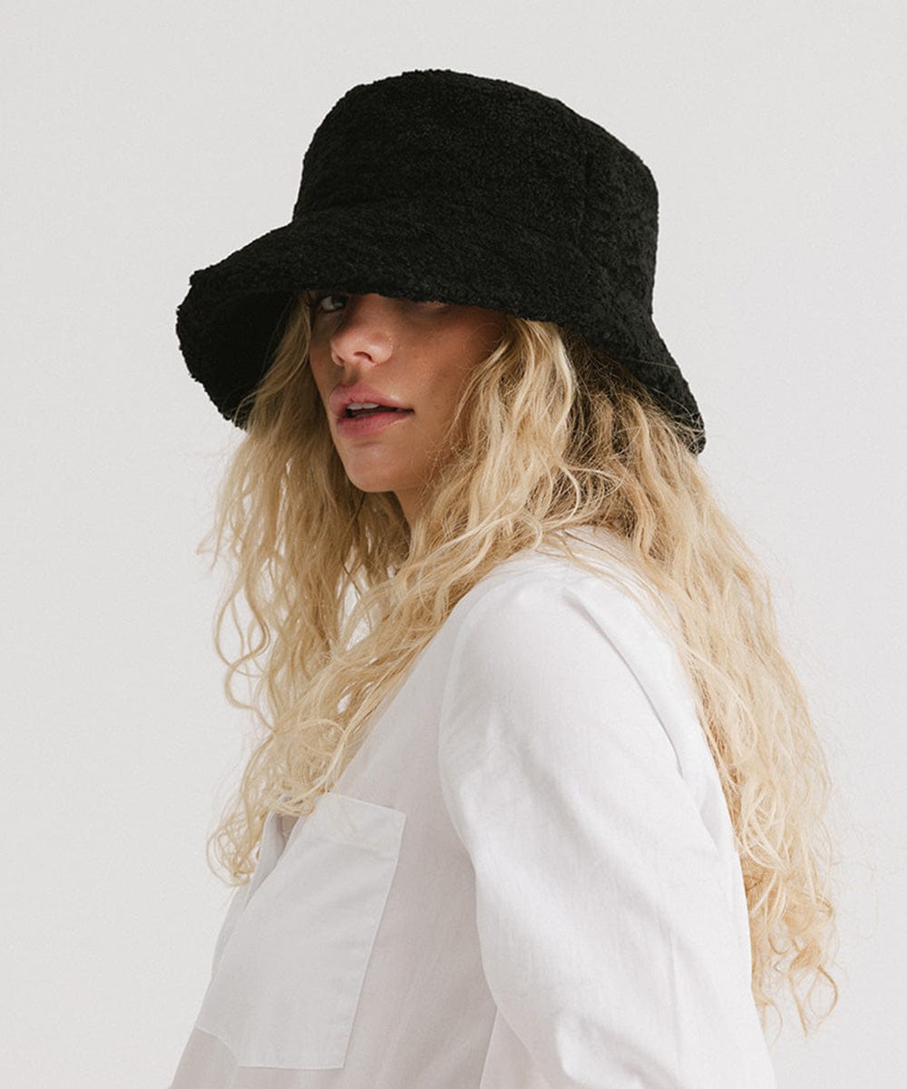 Woman wearing a black sherpa bucket hat and a white shirt against a plain background #color_black