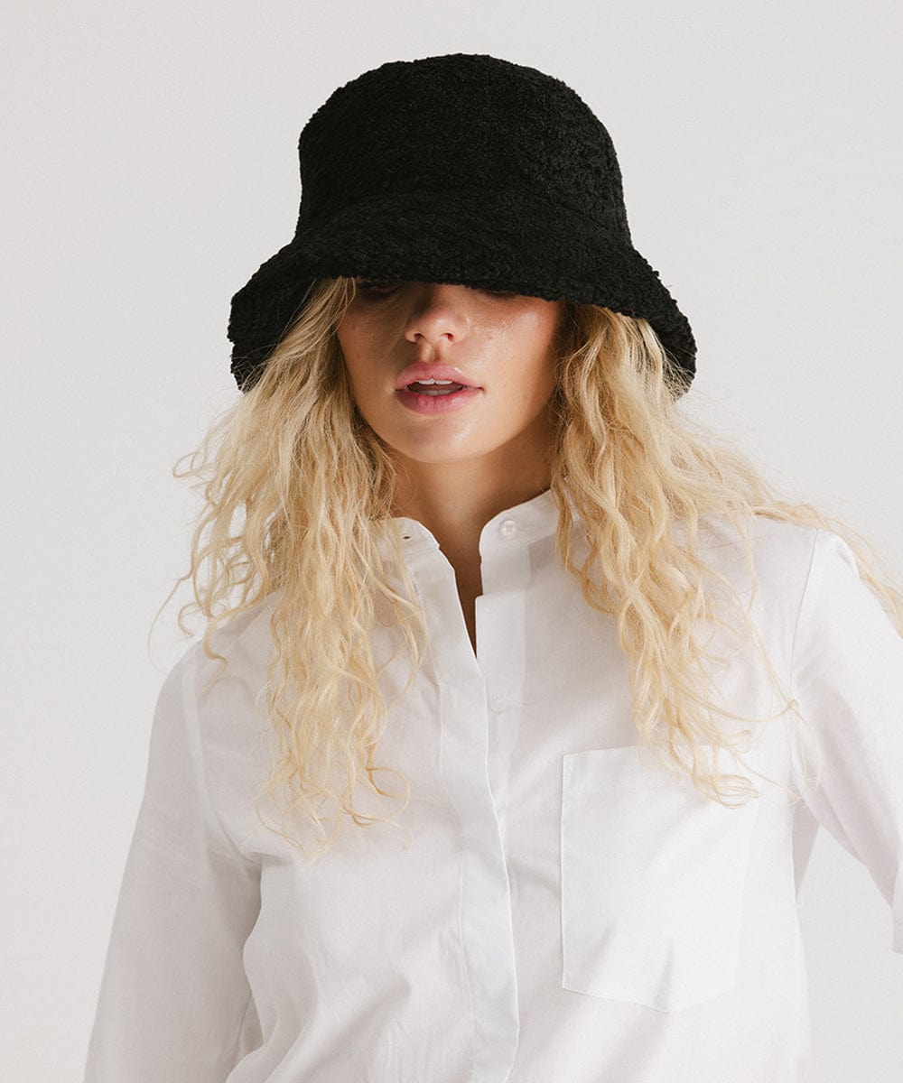 Woman wearing a black sherpa bucket hat and a white shirt against a plain background #color_black