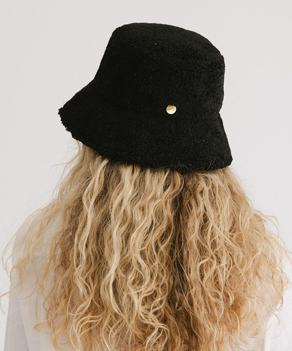 Person with long blonde hair wearing a black sherpa bucket hat against a plain background #color_black