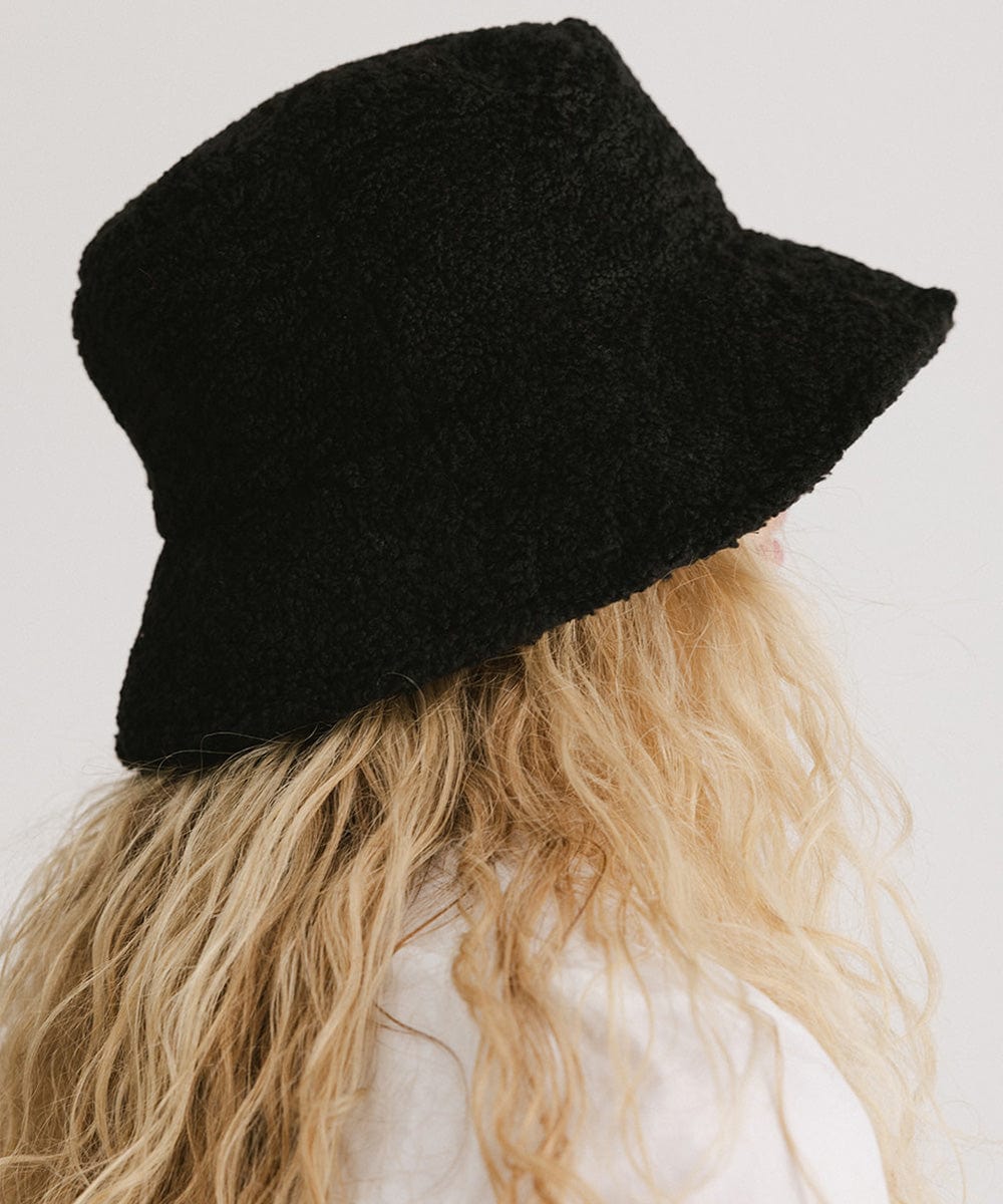 Person with blonde hair wearing a black sherpa bucket hat against a plain background #color_black