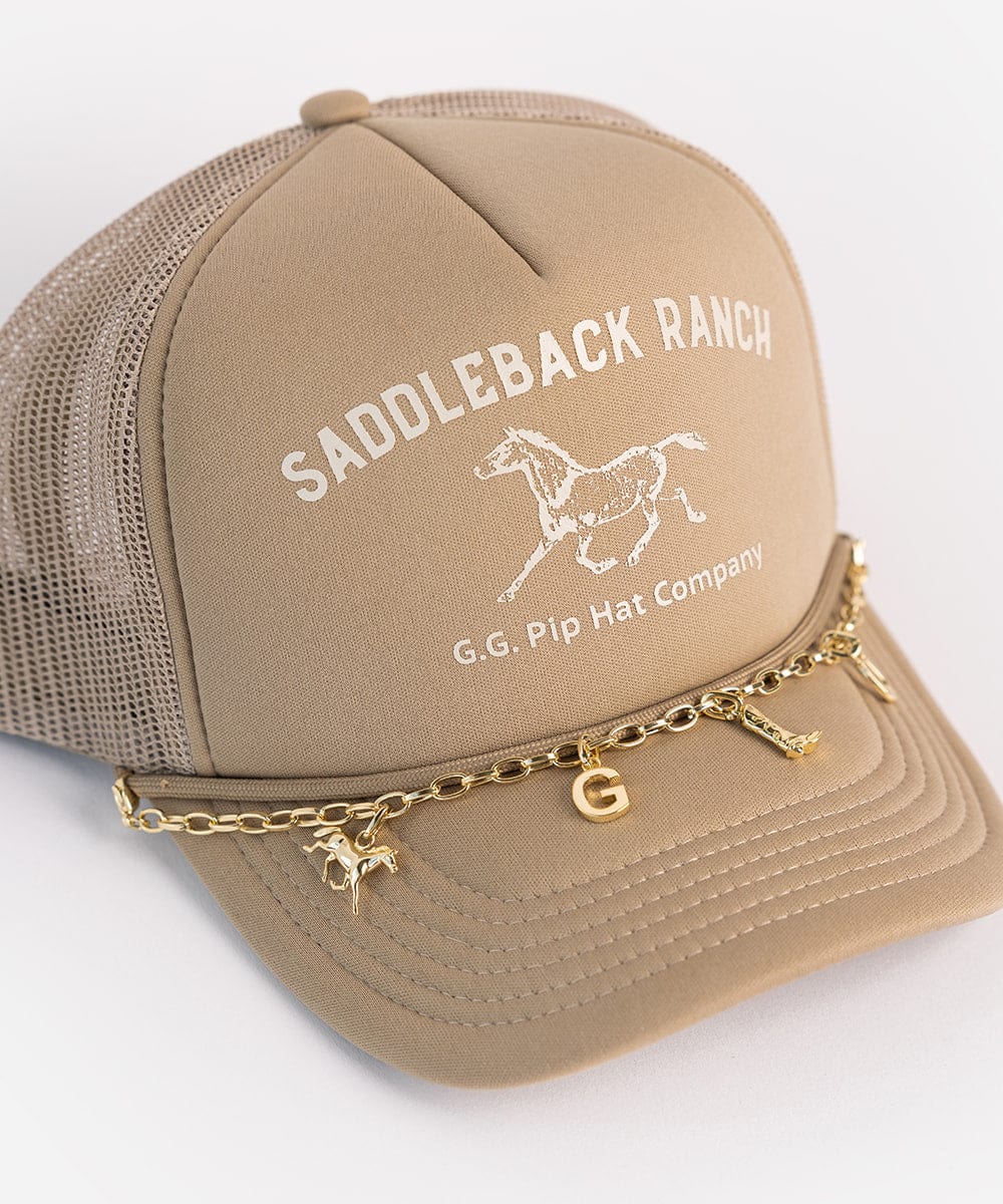 A beige cap with a horse logo and the text 'SADDLEBACK RANCH' and 'G.G. Pip Hat Company' and a gold chain with a gold cowboy boot hat charm, horse hat charm and letter 'G' hat charm on a white background #color_gold