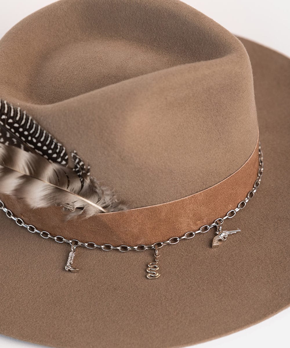 A brown hat with a band, two hat feathers and a silver chain with silver cowboy boot hat charm, snake hat charm and pistol hat charm on a white background #color_silver