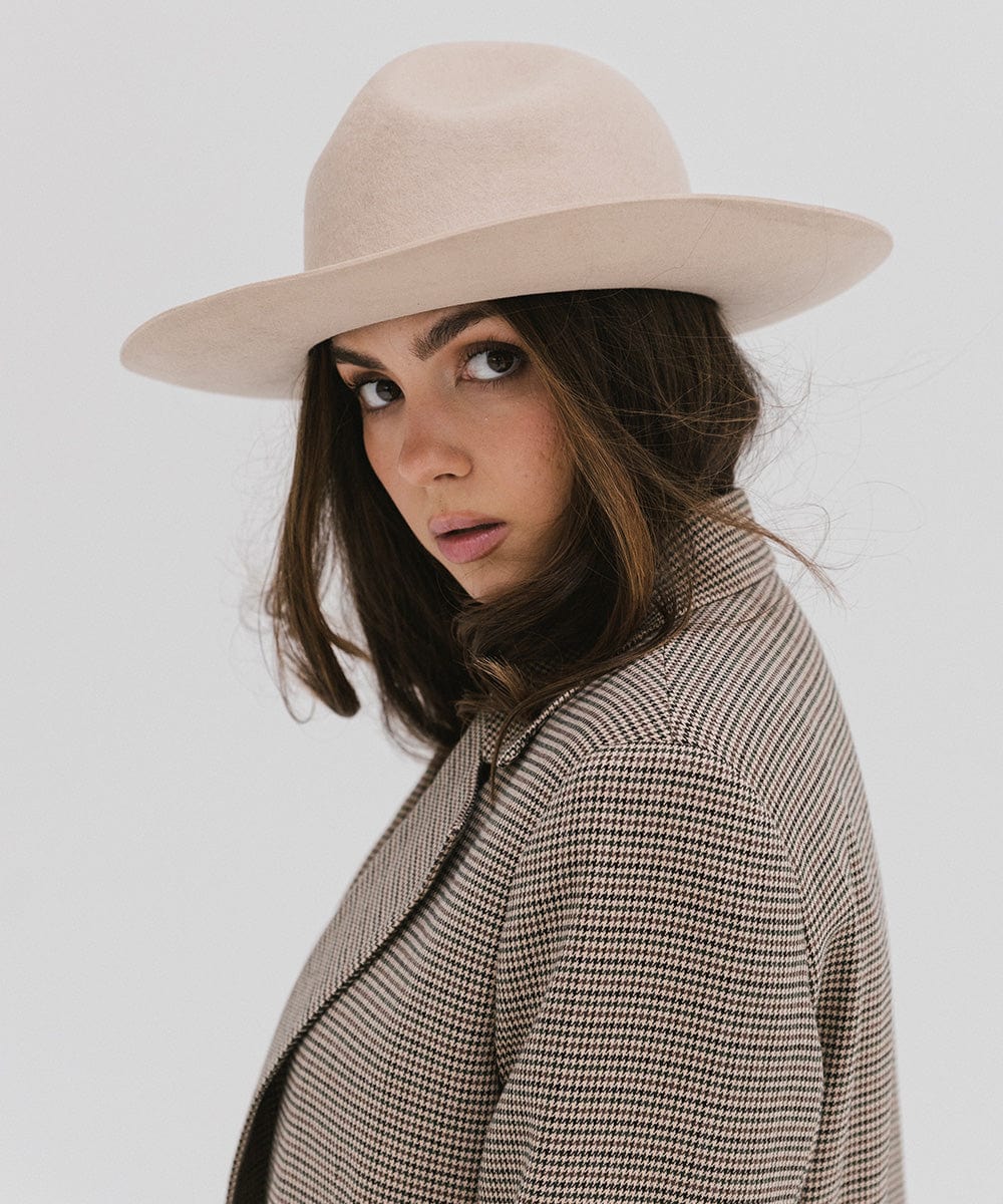 Woman wearing a cream fedora hat and a checkered coat, posing sideways against a plain background #color_cream