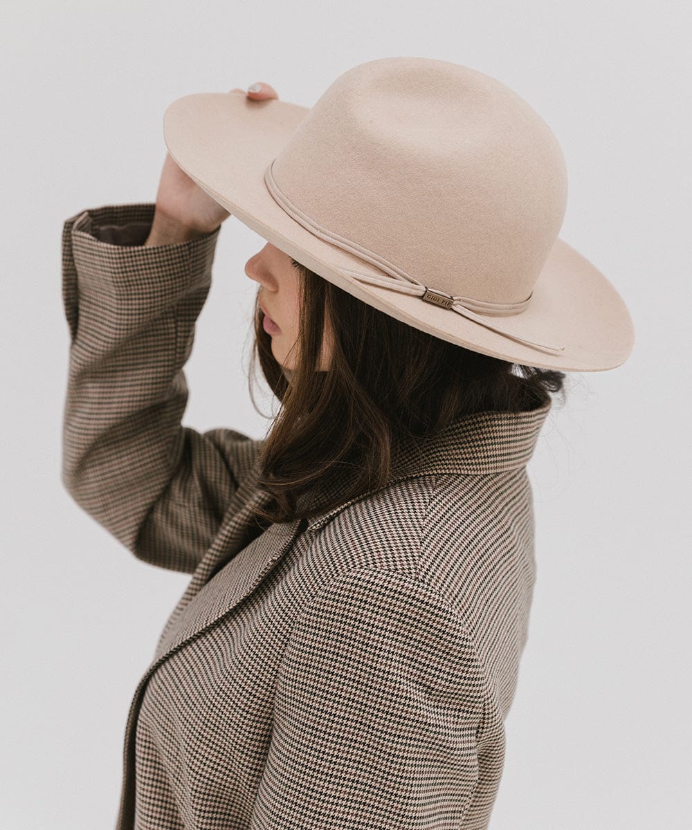 Woman wearing a cream fedora hat with a hat band and a checkered coat, facing sideways against a plain background #color_cream