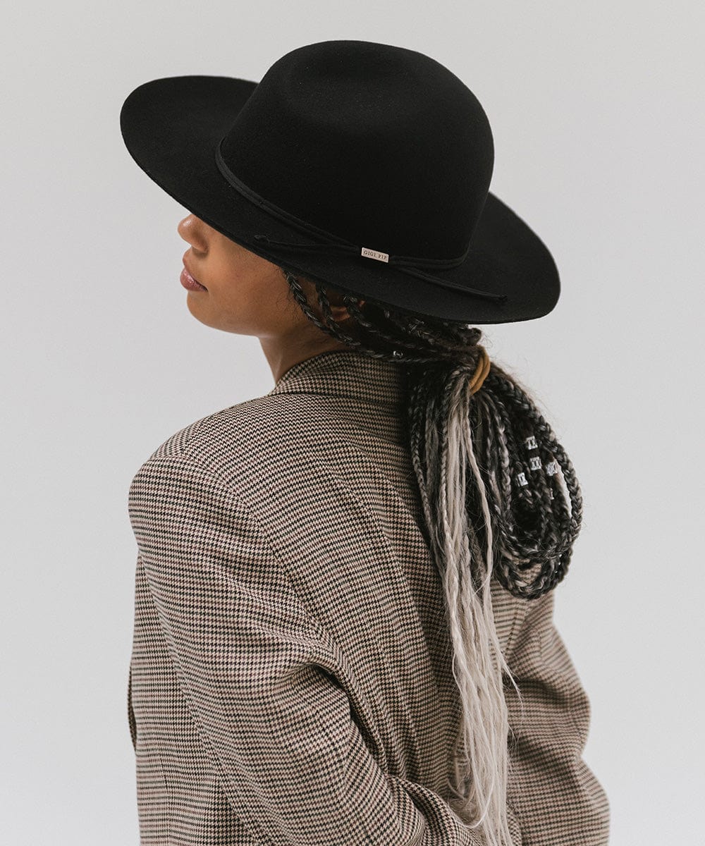 Woman wearing a black fedora hat with a hat band and a checkered coat, facing sideways against a plain background #color_black