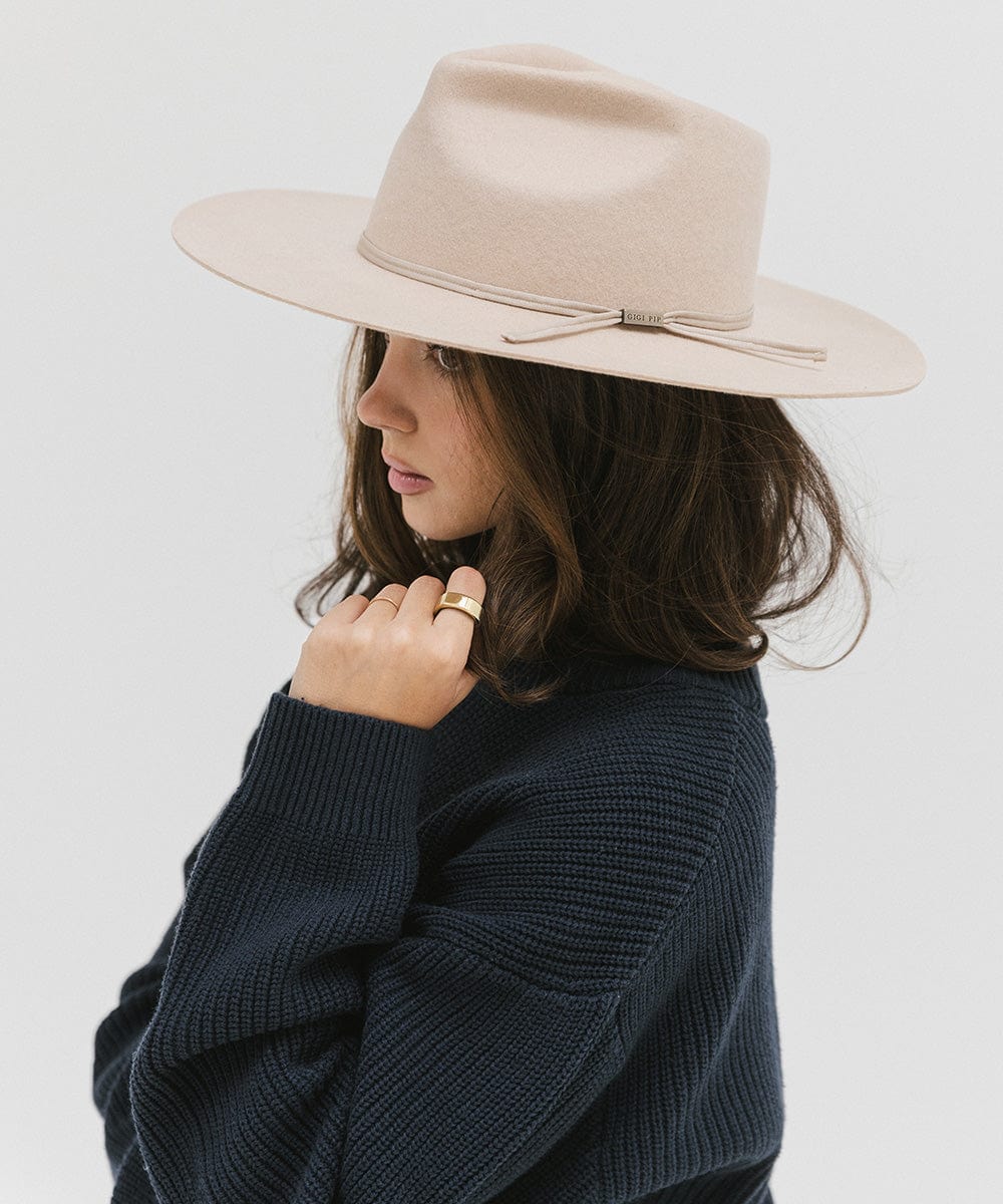 Woman wearing a cream fedora hat with a hat band and a dark blue sweatshirt, facing sideways against a plain background #color_cream