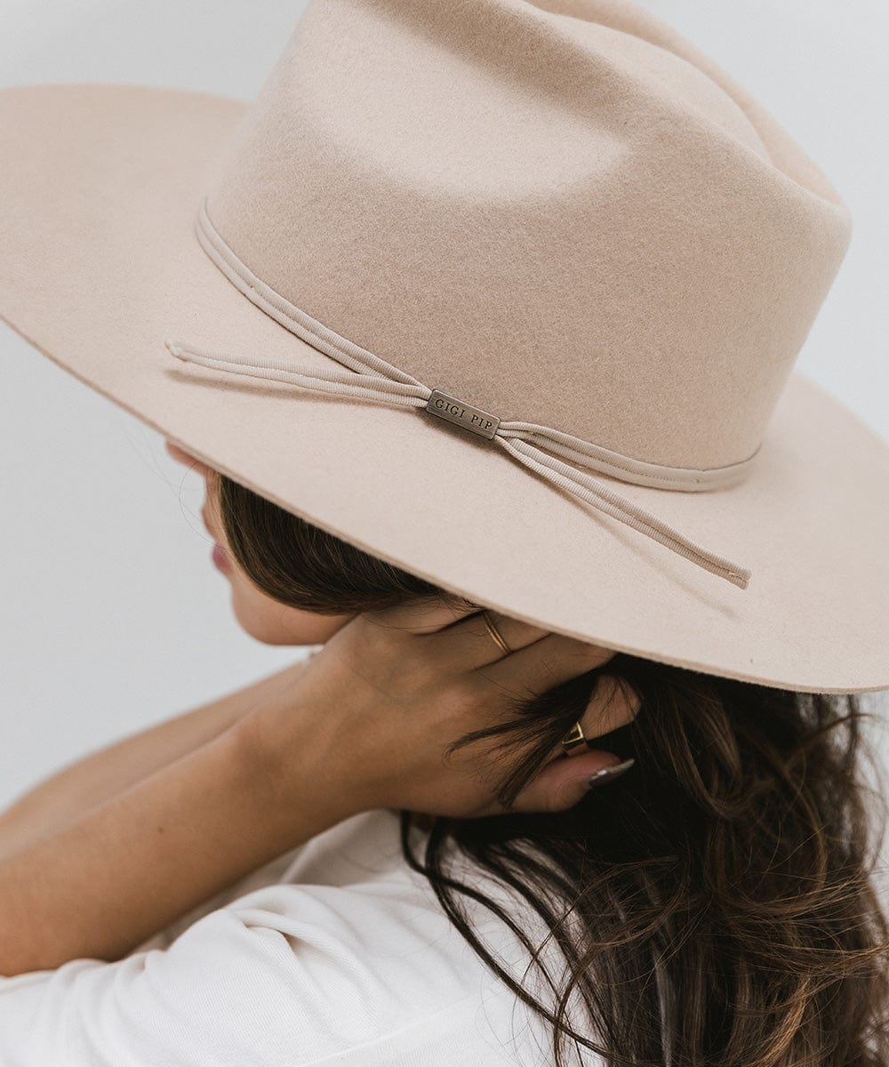 Woman wearing a cream fedora hat with a hat band against a plain background #color_cream