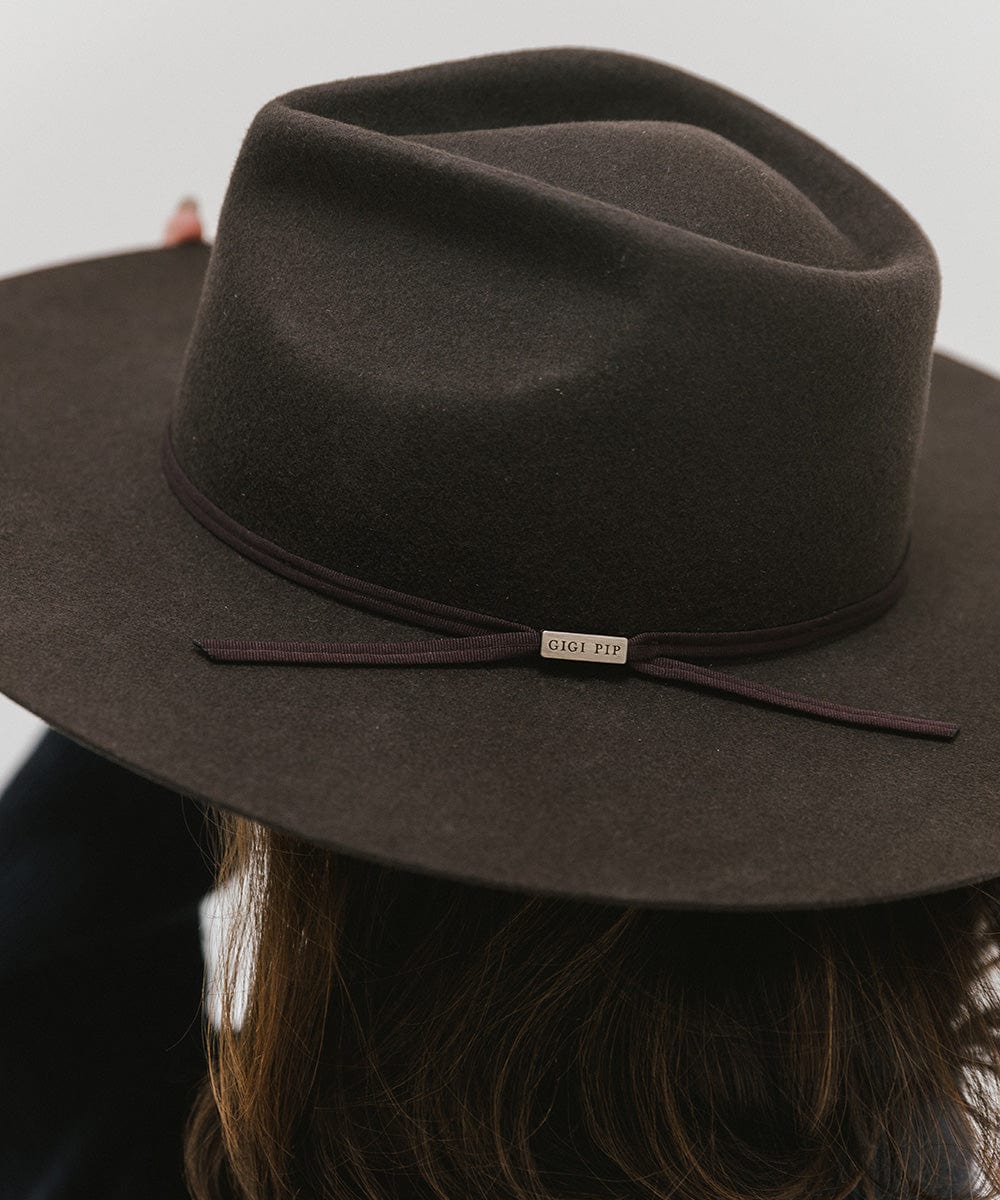 Person wearing a dark brown fedora hat with a hat band against a plain background #color_dark brown