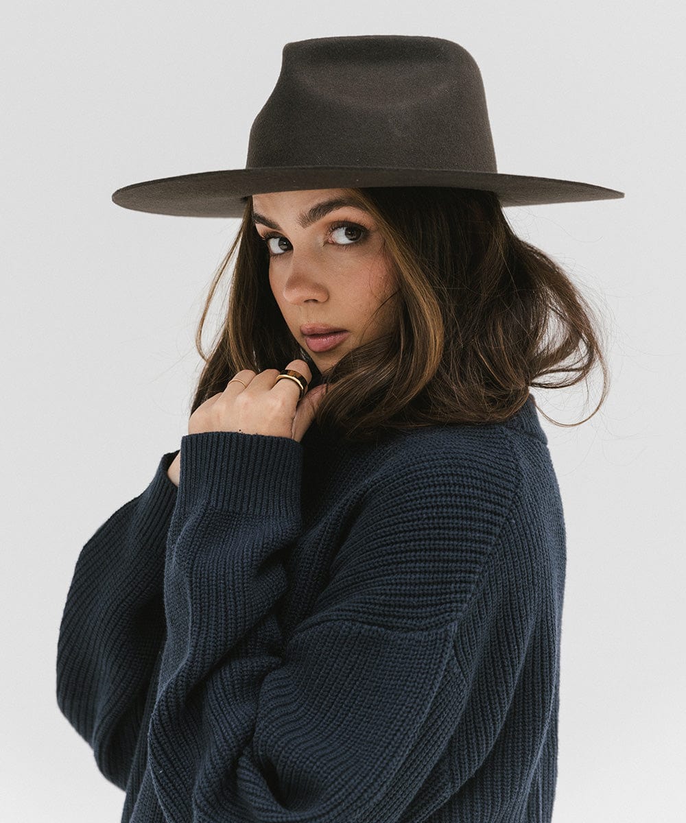 Woman wearing a dark brown fedora hat and a dark blue sweatshirt, posing against a plain background #color_dark brown