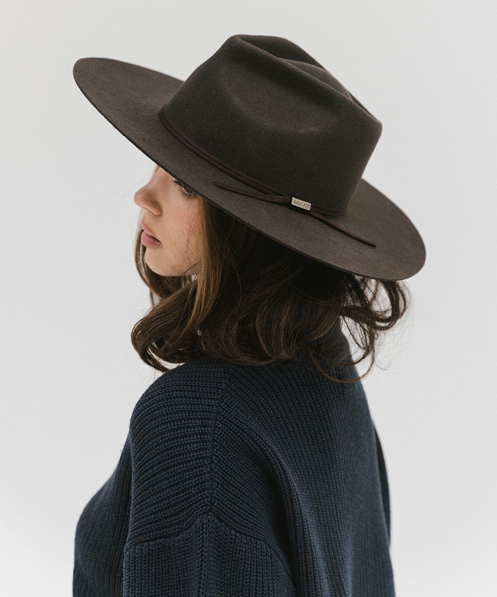 Woman wearing a dark brown fedora hat with a hat band and a dark blue sweatshirt, facing sideways against a plain background #color_dark brown