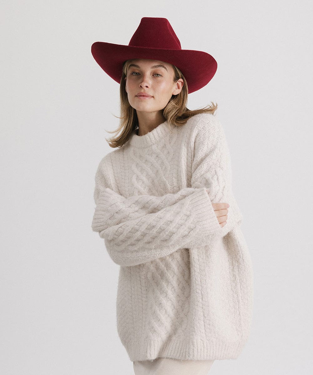 Woman wearing a burgundy colored felt hat and a white sweater against a plain background  #color_burgundy