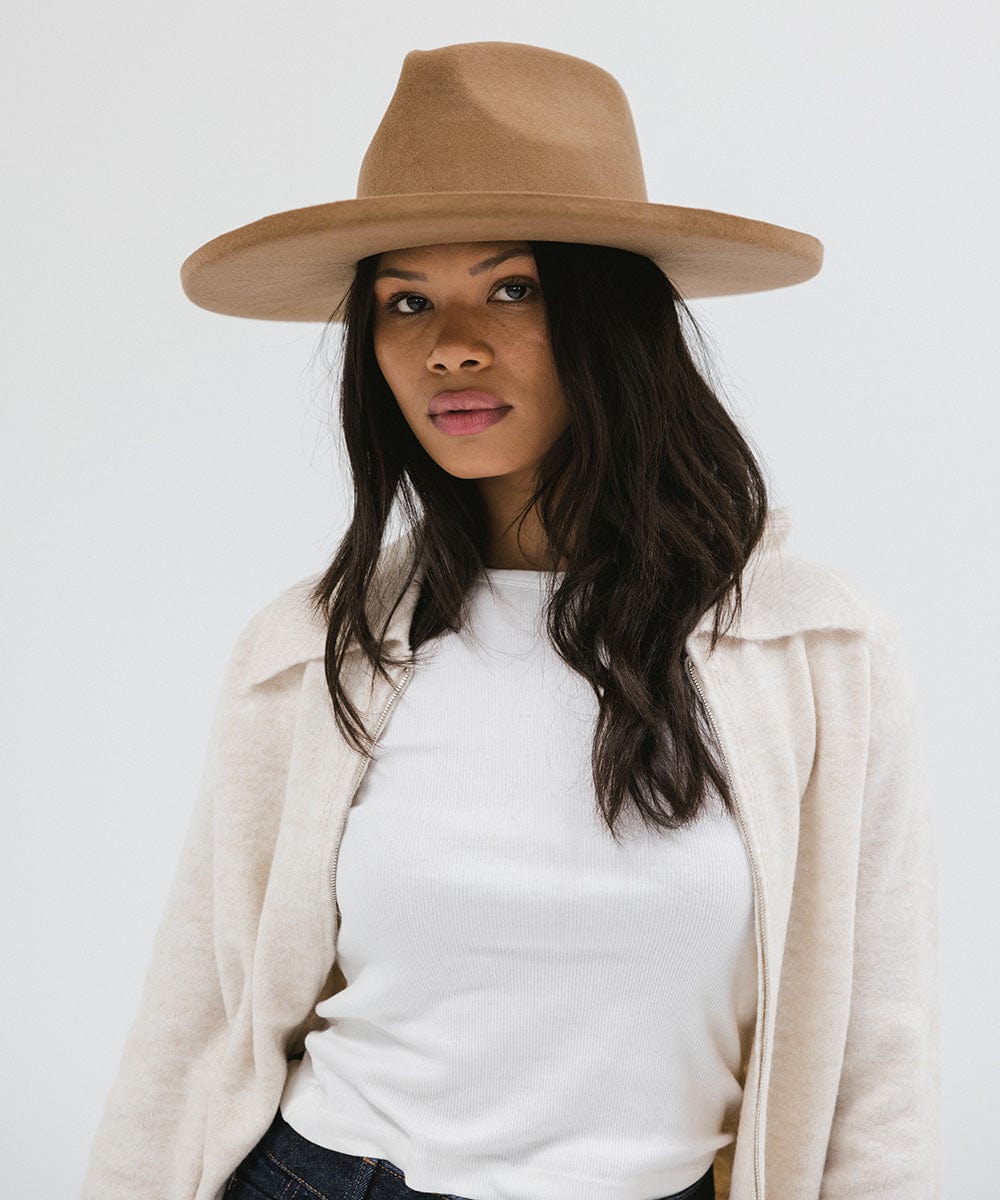 Woman wearing a brown pencil brim fedora hat and a white top with a cream jacket against a white background #color_brown