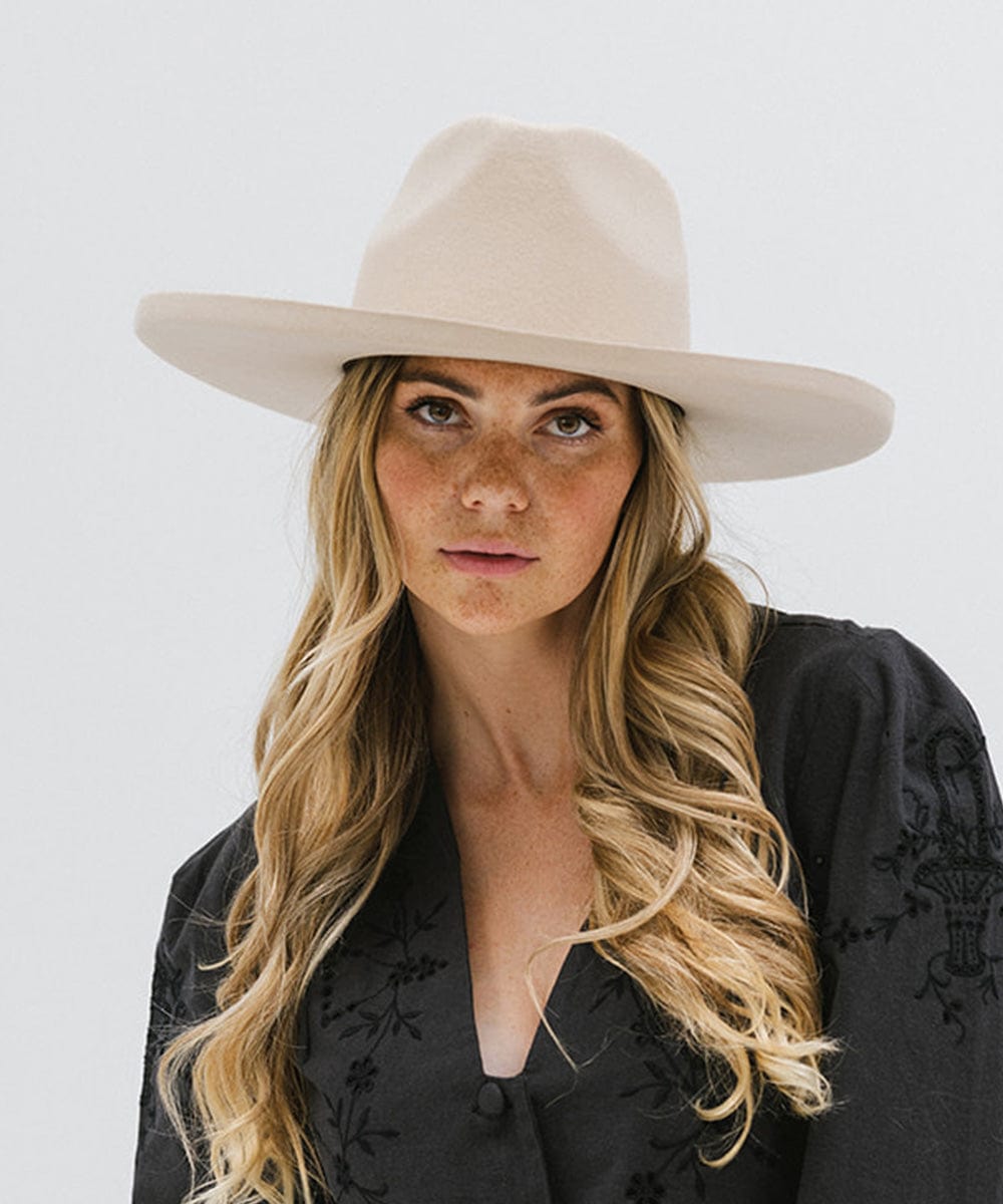 Woman wearing a cream colored pencil brim fedora hat with a wide brim and a black printed shirt against a white background #color_cream