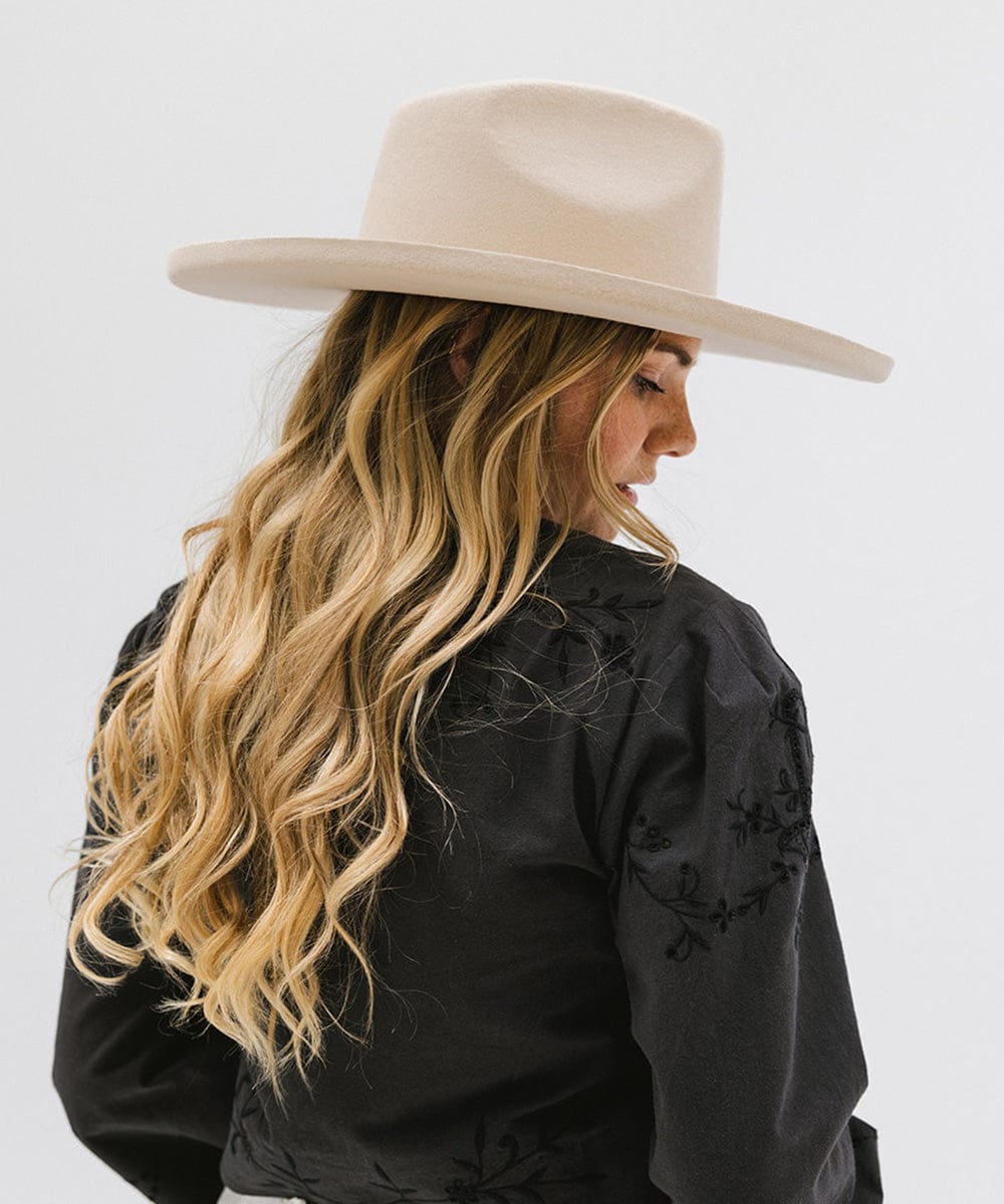 Woman wearing a cream colored pencil brim fedora hat with a wide brim and a black printed shirt, facing sideways against a white background #color_cream