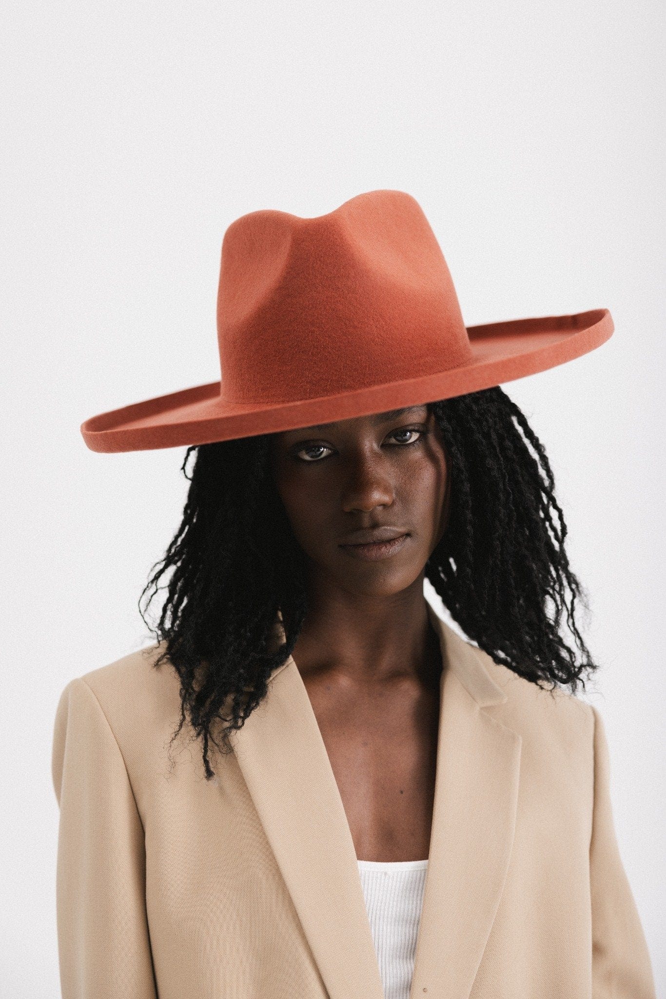 Woman wearing a clay colored pencil brim fedora hat with a wide brim and a light brown blazer against a white background #color_clay