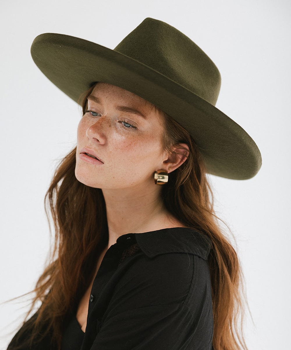 Woman wearing a moss colored pencil brim fedora hat with a wide brim and a black shirt, looking sideways against a white background #color_limited edition moss