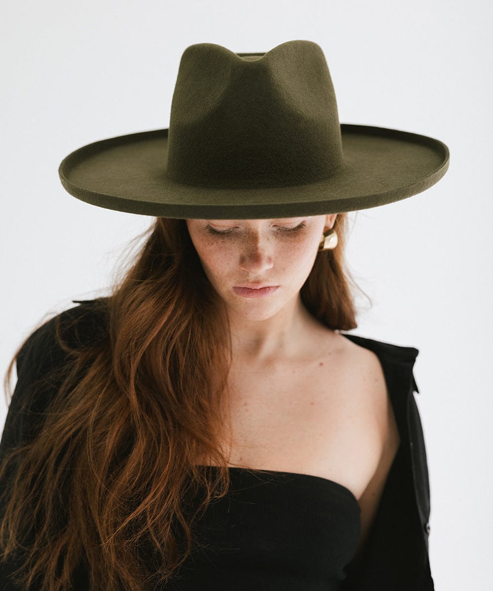 Woman wearing a moss colored pencil brim fedora hat with a wide brim and a black top against a white background #color_limited edition moss