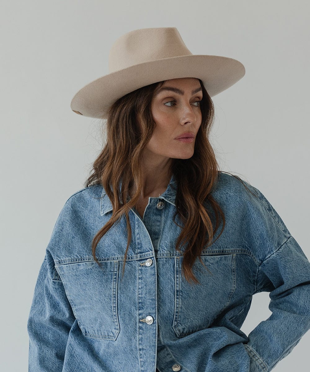 Woman wearing a cream fedora hat and a denim shirt, looking sideways against a plain background #color_cream