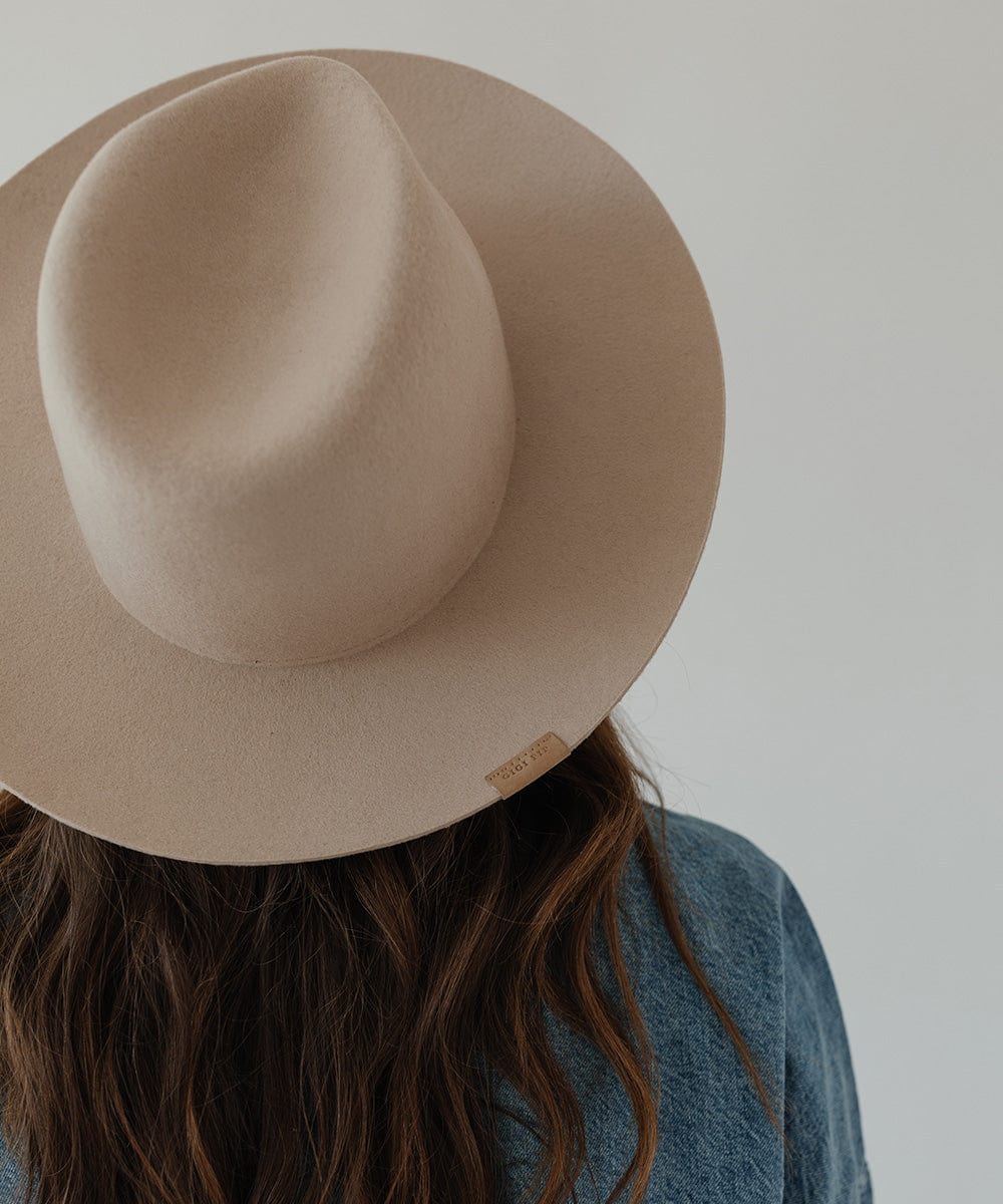 Woman wearing a cream fedora hat facing behind against a plain background #color_cream