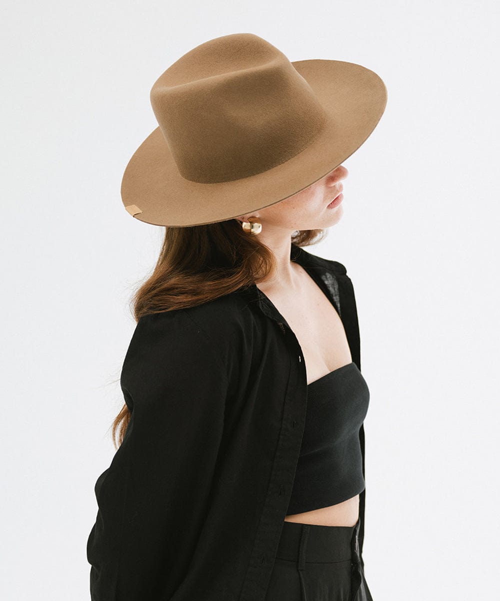 Woman wearing a brown fedora hat and a lack top with a black shirt, facing sideways against a plain background #color_brown