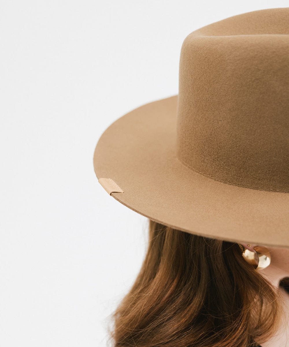 Close up image of someone wearing a brown fedora hat against a plain background #color_brown