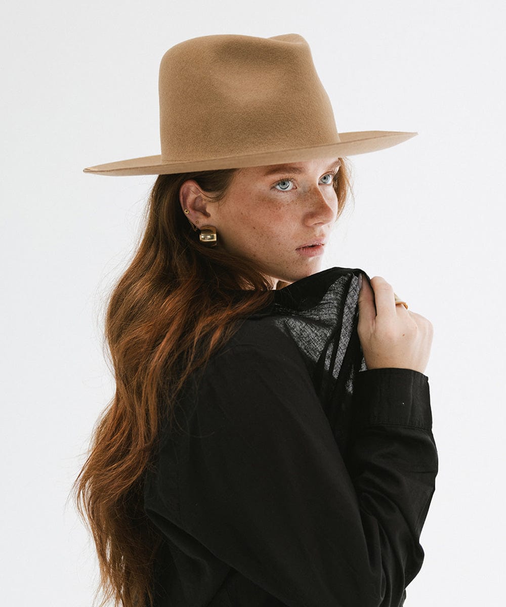 Woman wearing a brown fedora hat and a lack top with a black shirt, posing sideways against a plain background #color_brown