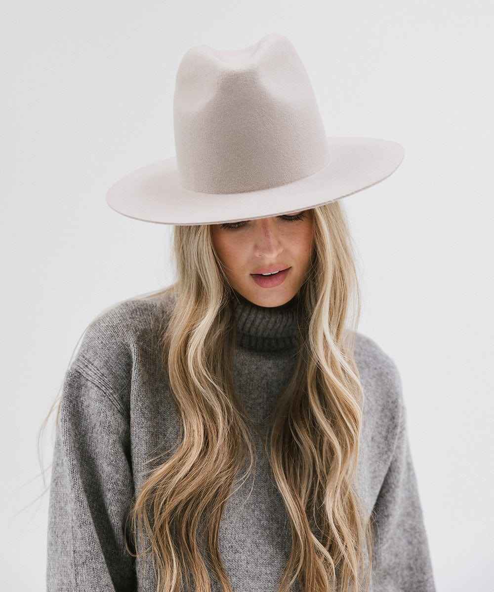 Woman wearing an ivory colored hat and grey sweater, looking down against a white background #color_ivory