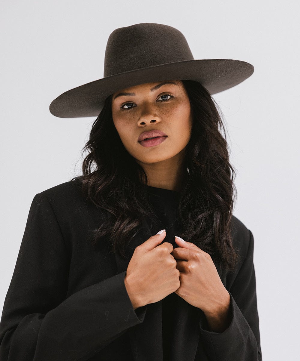 Woman wearing a dark brown wide brim felt hat with a triangle crown and a black blazer against a white background #color_dark brown