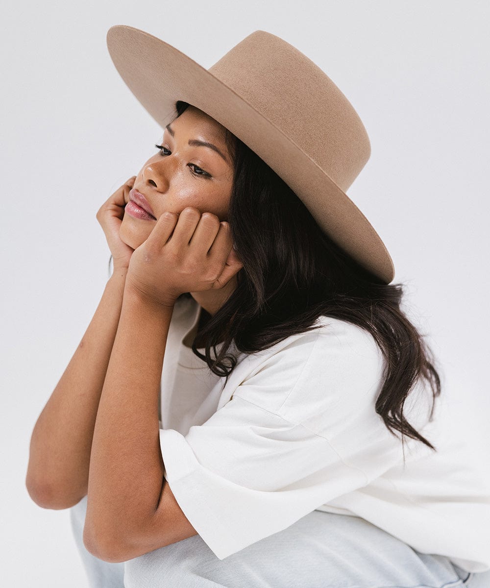 Woman wearing a brown wide brim felt hat with a triangle crown and a white shirt, looking sideways against a white background #color_brown