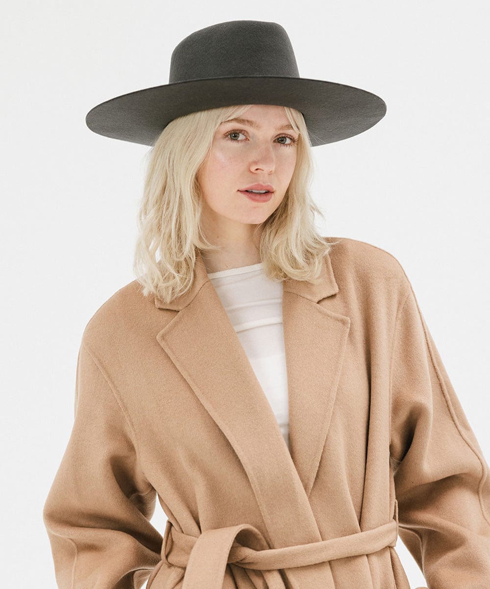 Woman wearing a dark grey wide brim felt hat with a triangle crown and a brown jacket against a white background #color_dark grey