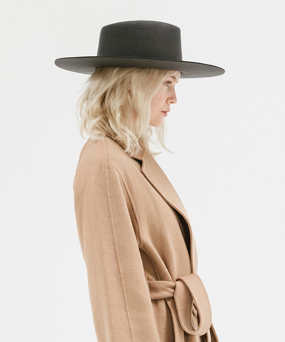 Woman wearing a dark grey wide brim felt hat with a triangle crown and a brown jacket, facing sideways against a white background #color_dark grey
