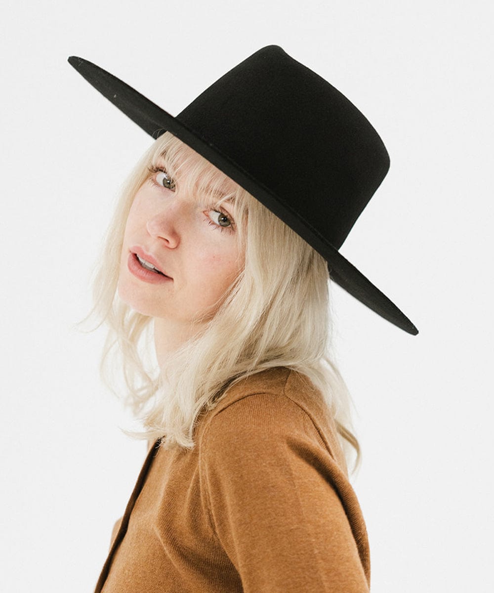 Woman wearing a black wide brim felt hat with a triangle crown and a brown shirt against a white background #color_black