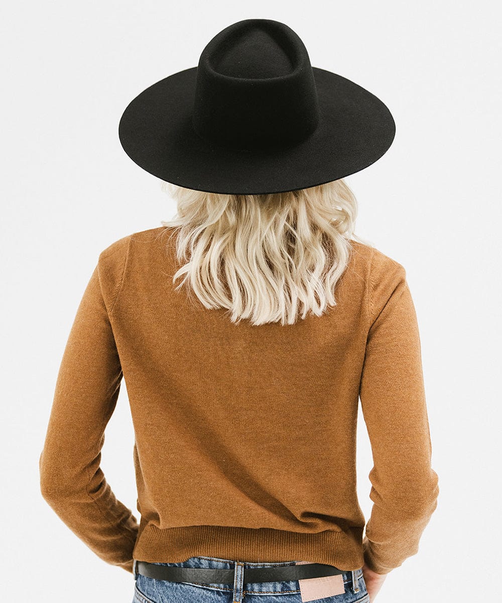 Woman wearing a black wide brim felt hat with a triangle crown and a brown shirt, facing behind against a white background #color_black