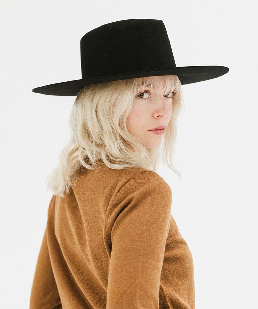 Woman wearing a black wide brim felt hat with a triangle crown and a brown shirt, posing against a white background #color_black