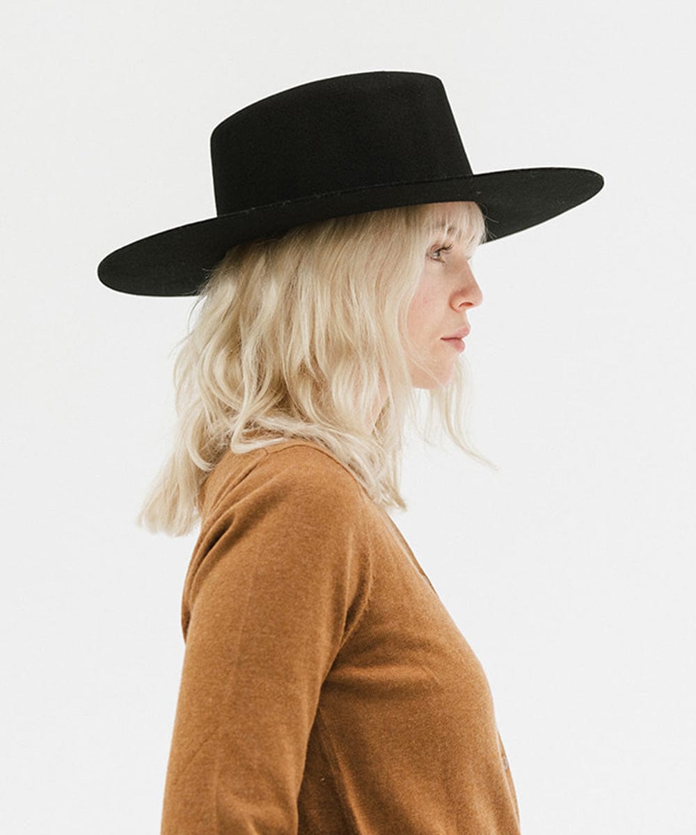 Woman wearing a black wide brim felt hat with a triangle crown and a brown shirt, facing sideways against a white background #color_black