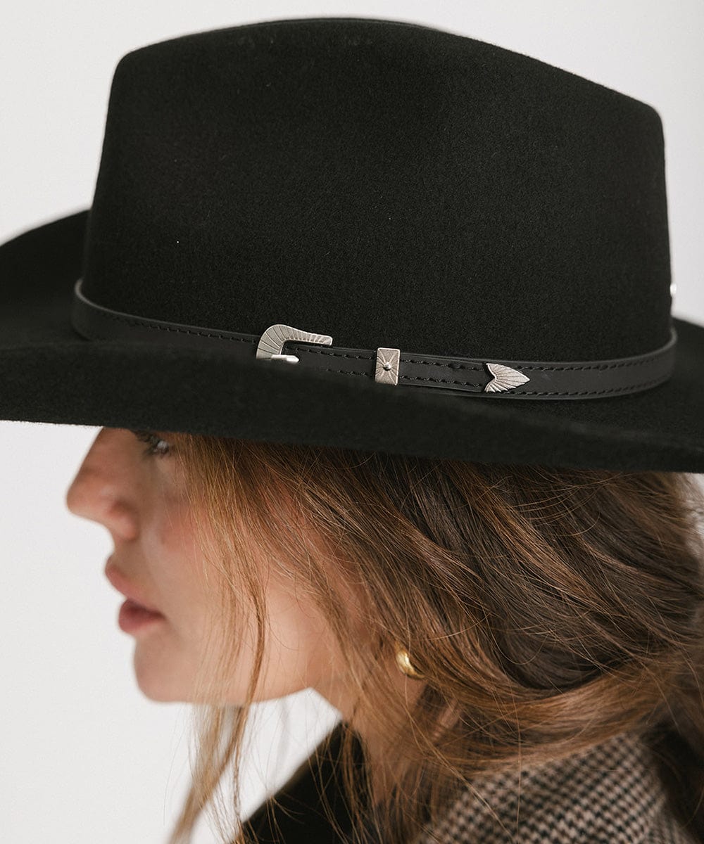 Woman wearing a black cowboy hat with a hat band looking sideways against a plain background  #color_black