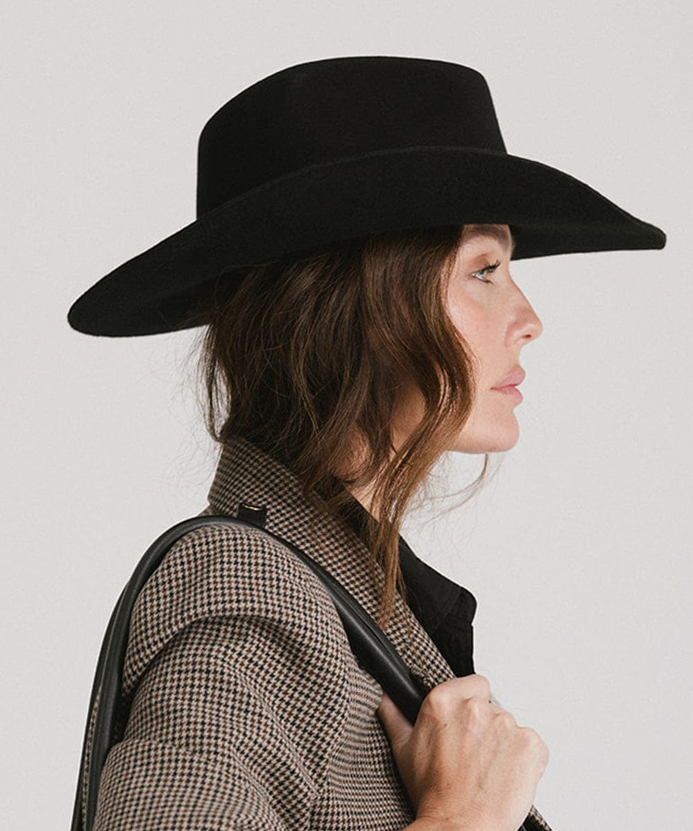 Woman wearing a black cowboy hat  and a blazer, facing sideways against a plain background  #color_black