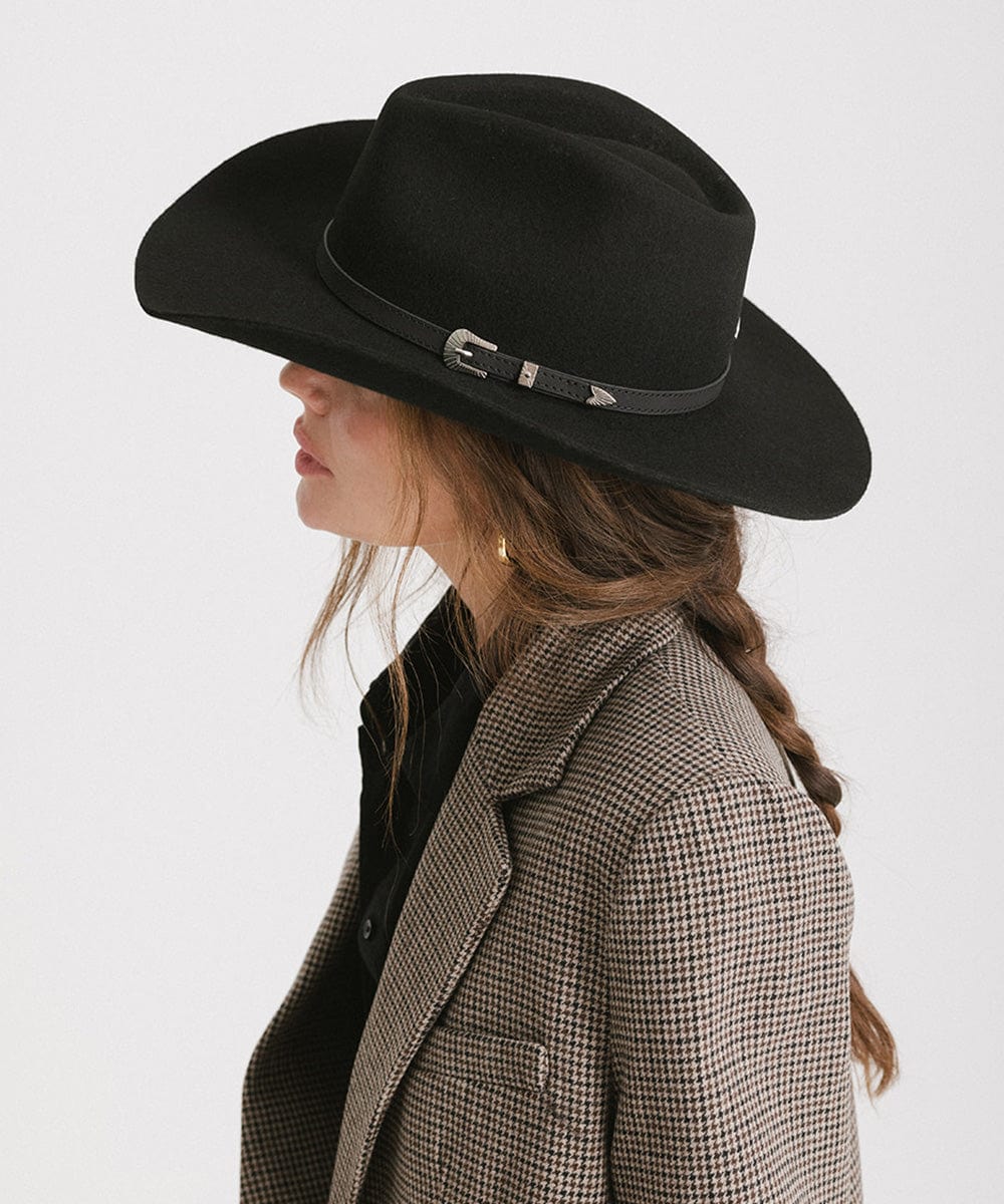 Woman wearing a black cowboy hat with a hat band and a blazer, facing sideways against a plain background  #color_black