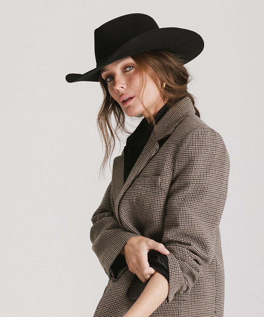 Woman wearing a black cowboy hat  and a blazer against a plain background  #color_black
