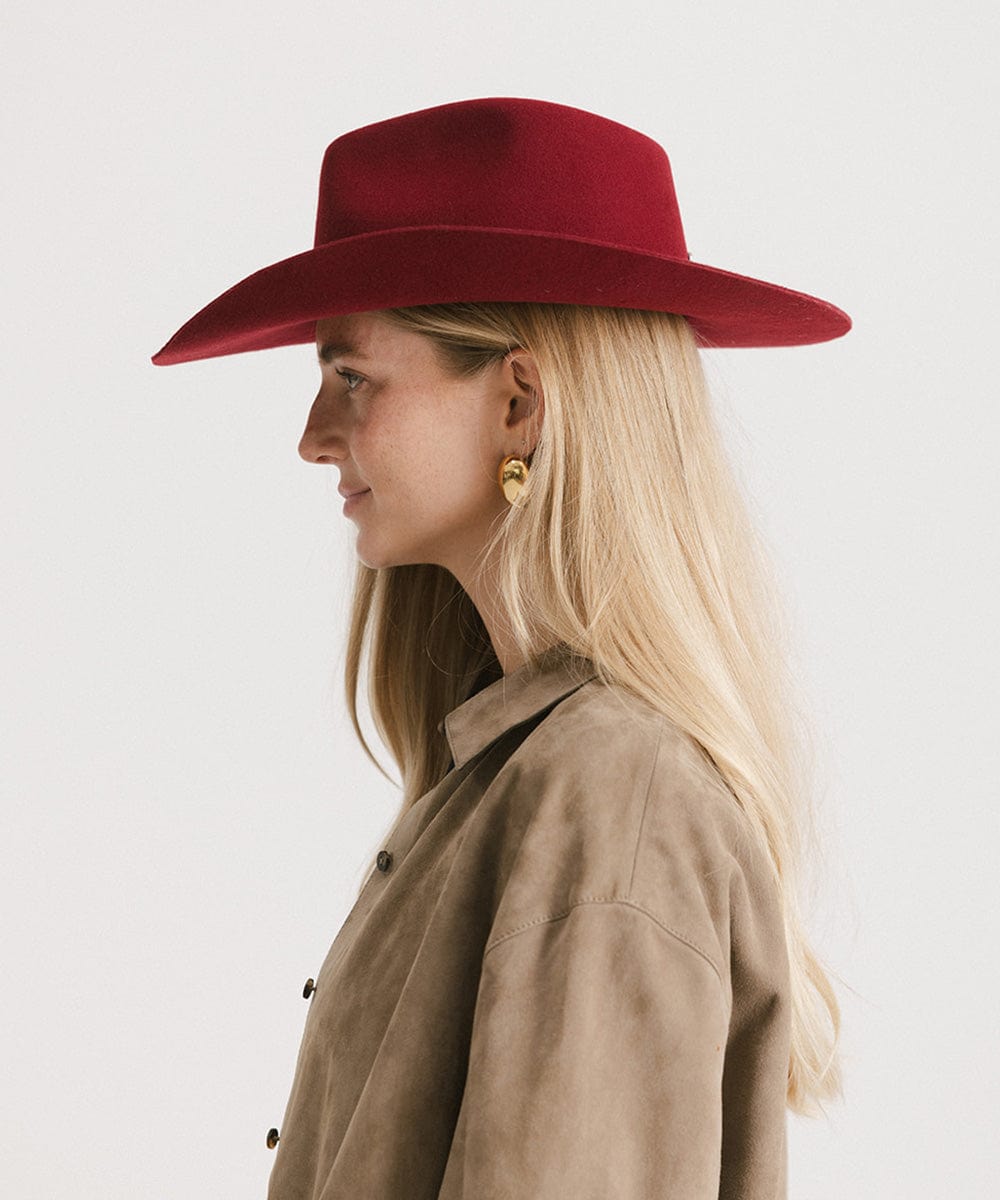 Woman wearing a burgundy cowboy hat and a beige shirt, facing sideways against a plain background #color_burgundy