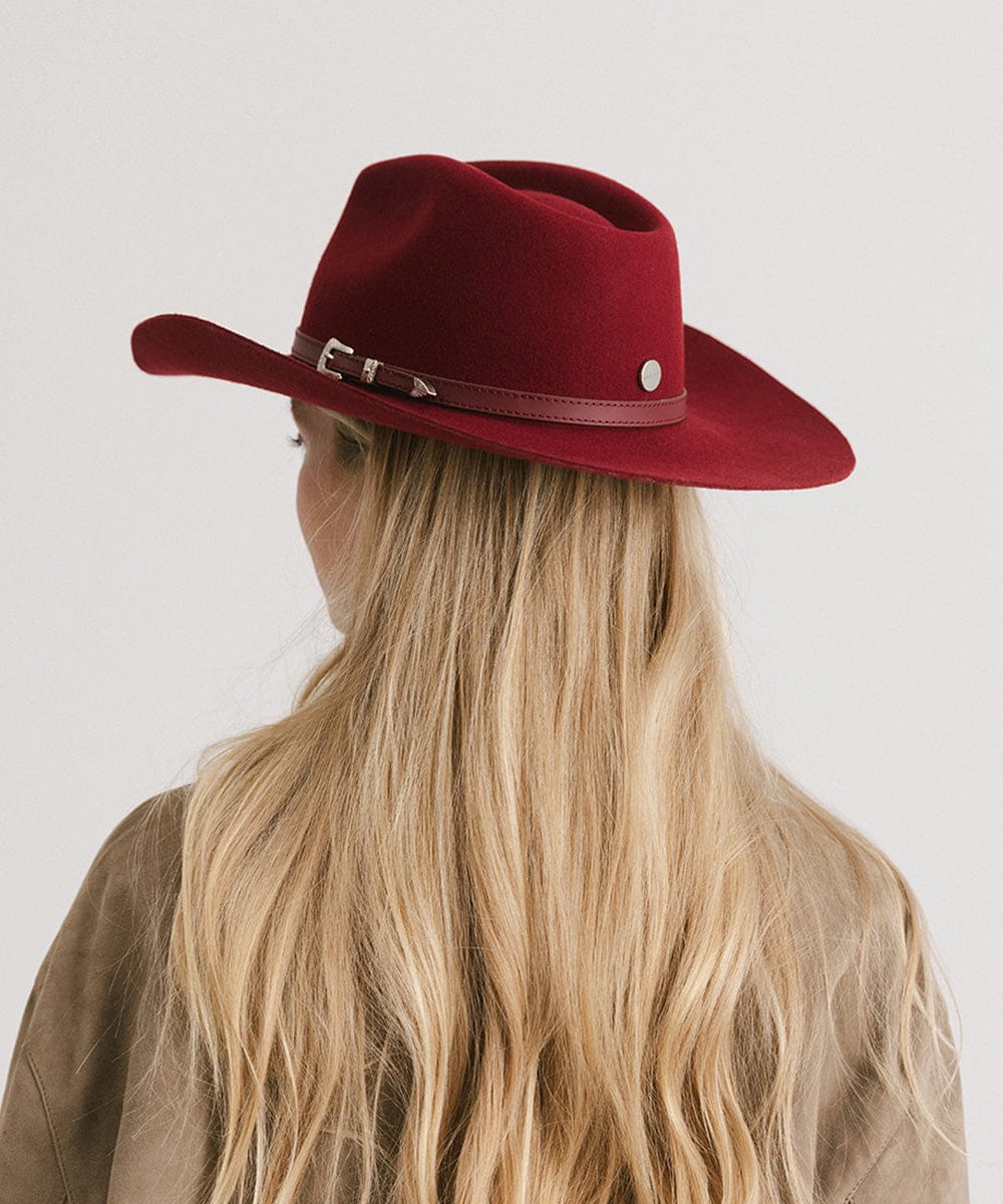 Woman wearing a burgundy cowboy hat with a hat band and a beige shirt, facing behind against a plain background #color_burgundy