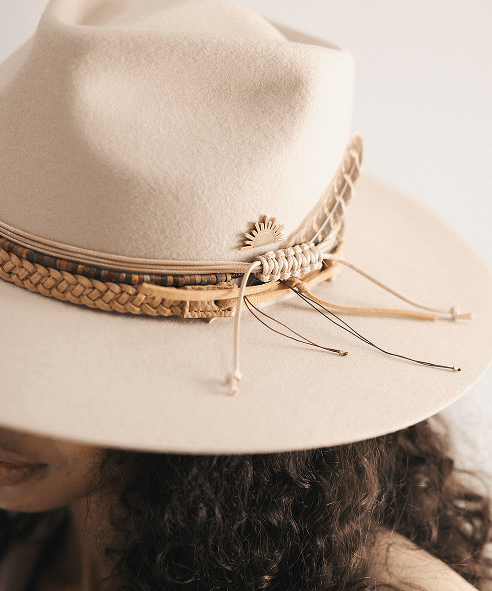 Woman wearing a beige cowboy hat with braided detail against a white background #color_tan