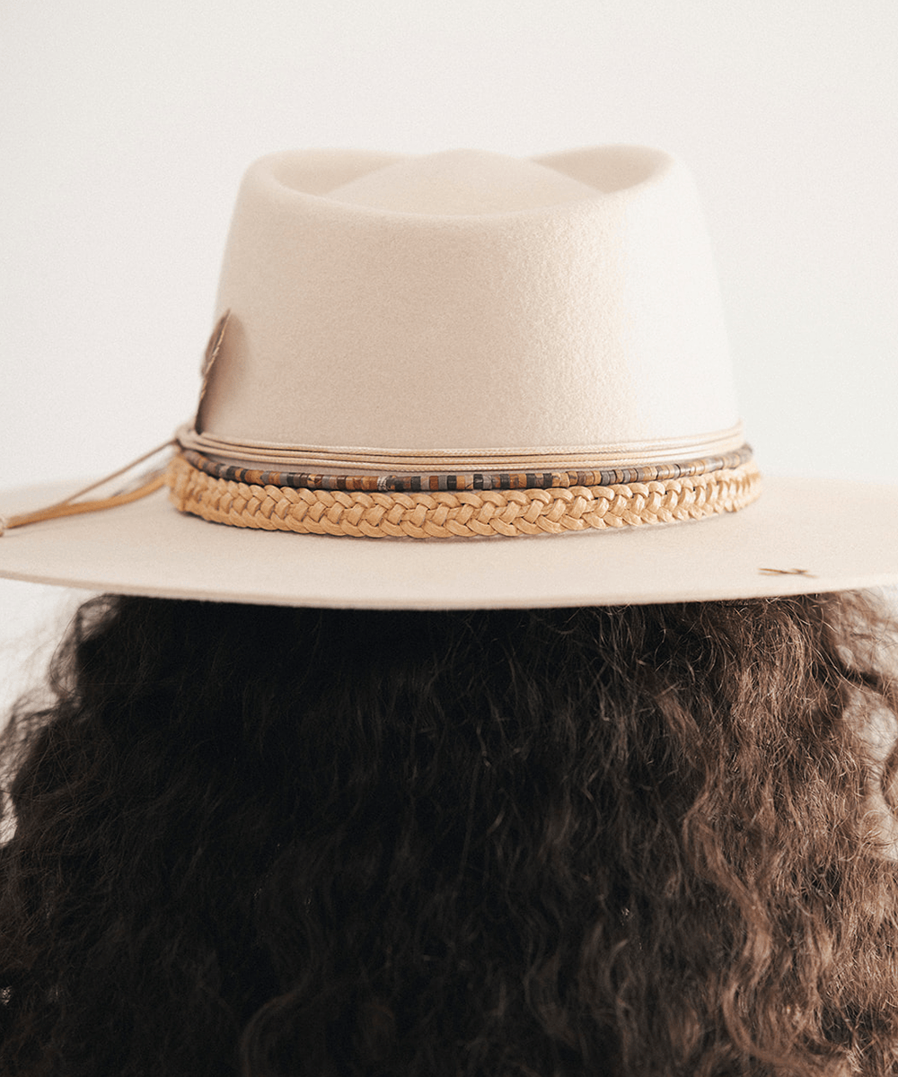 Woman wearing a beige cowboy hat with braided detail against a white background #color_tan