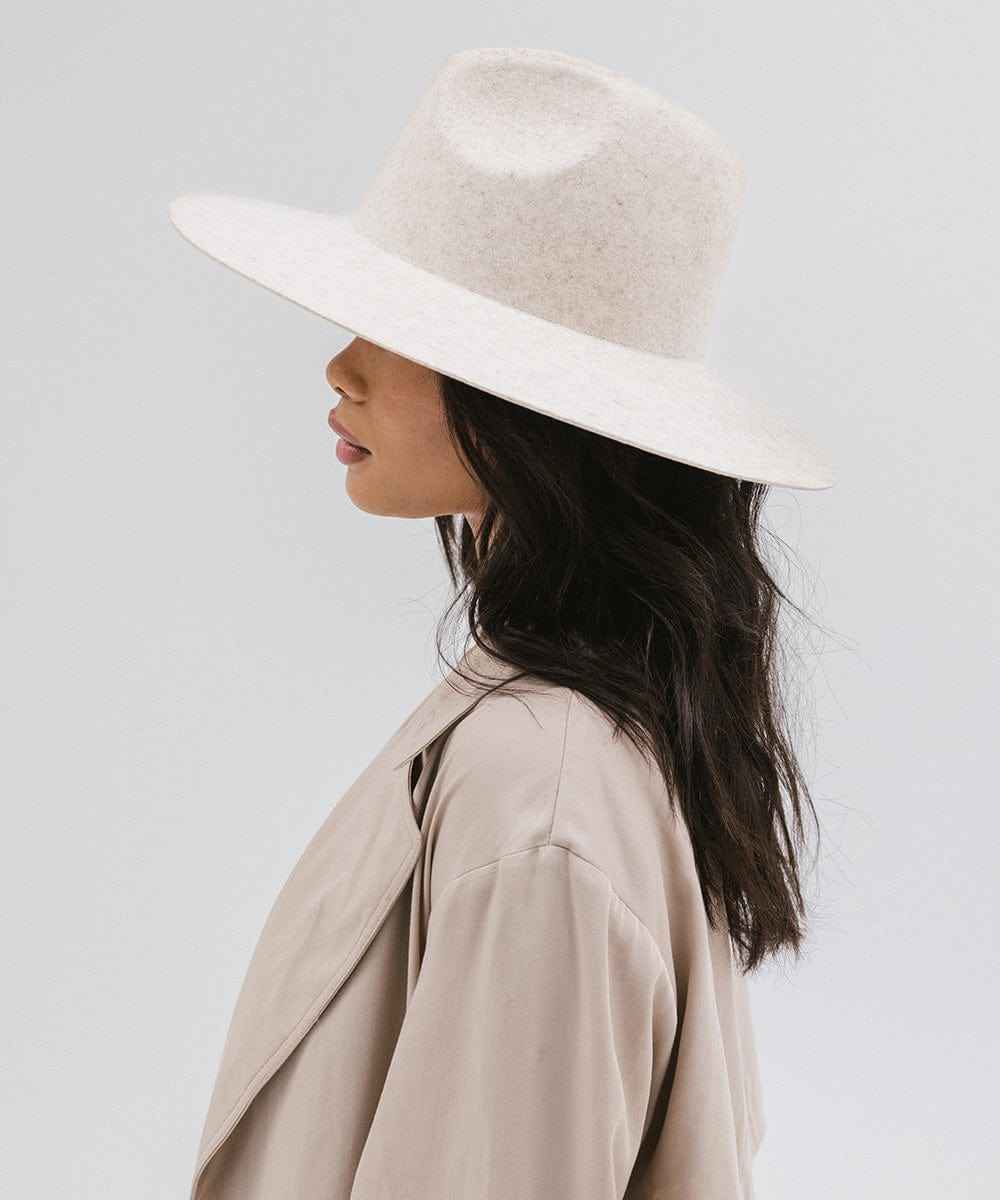 Woman wearing a mix ivory colored wide brim hat and a beige coat, facing sideways against a plain background #color_mix ivory