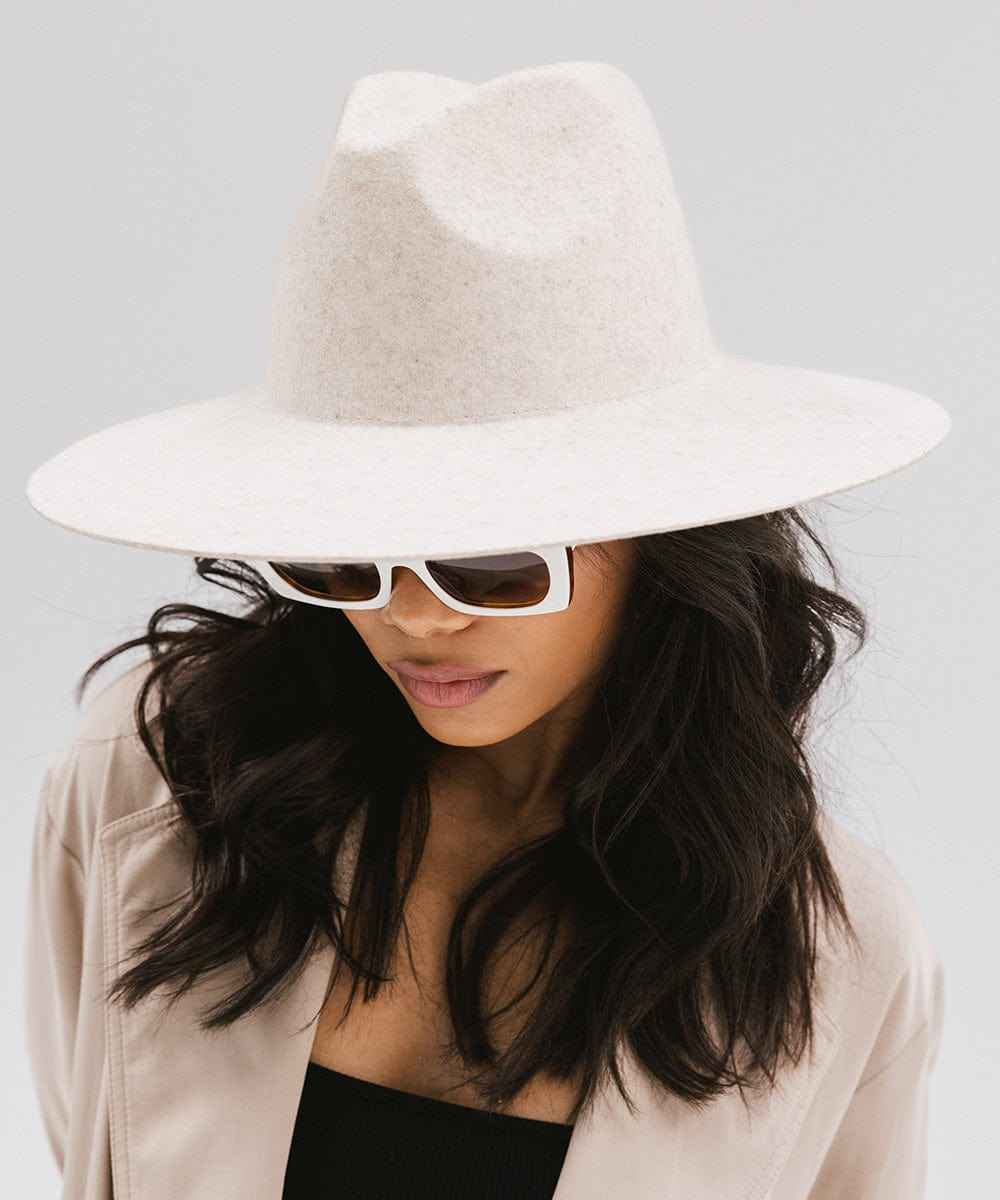 Woman wearing a mix ivory colored wide brim hat, sunglasses, and a beige coat against a plain background #color_mix ivory