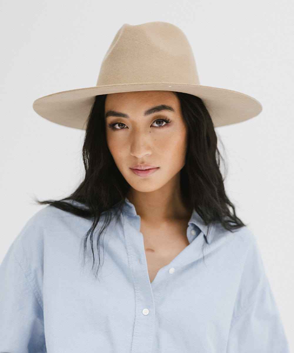 Woman wearing a tan wide brim fedora hat and a blue shirt against a plain background #color_tan