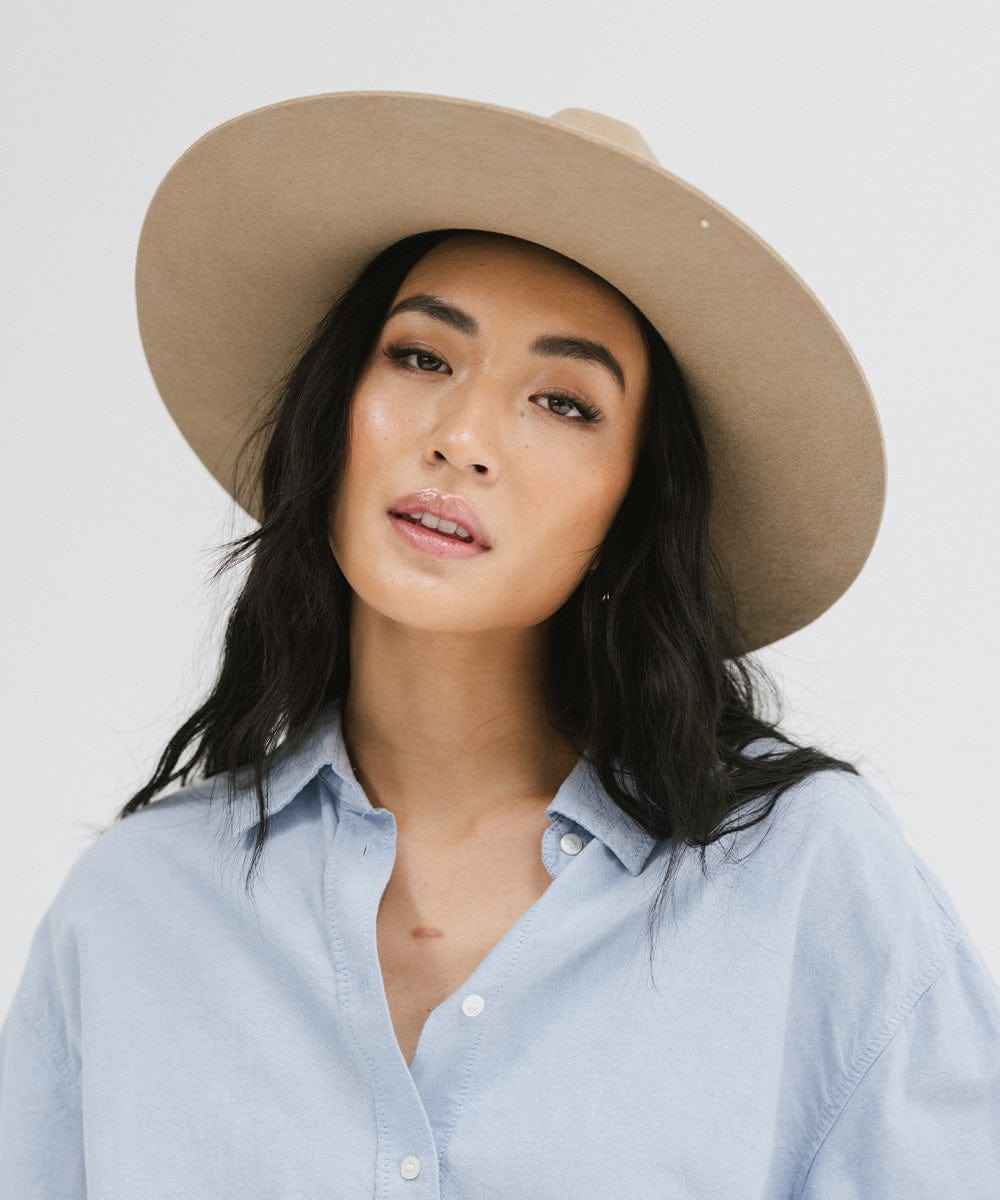 Woman wearing a tan wide brim fedora hat and a blue shirt against a plain background #color_tan