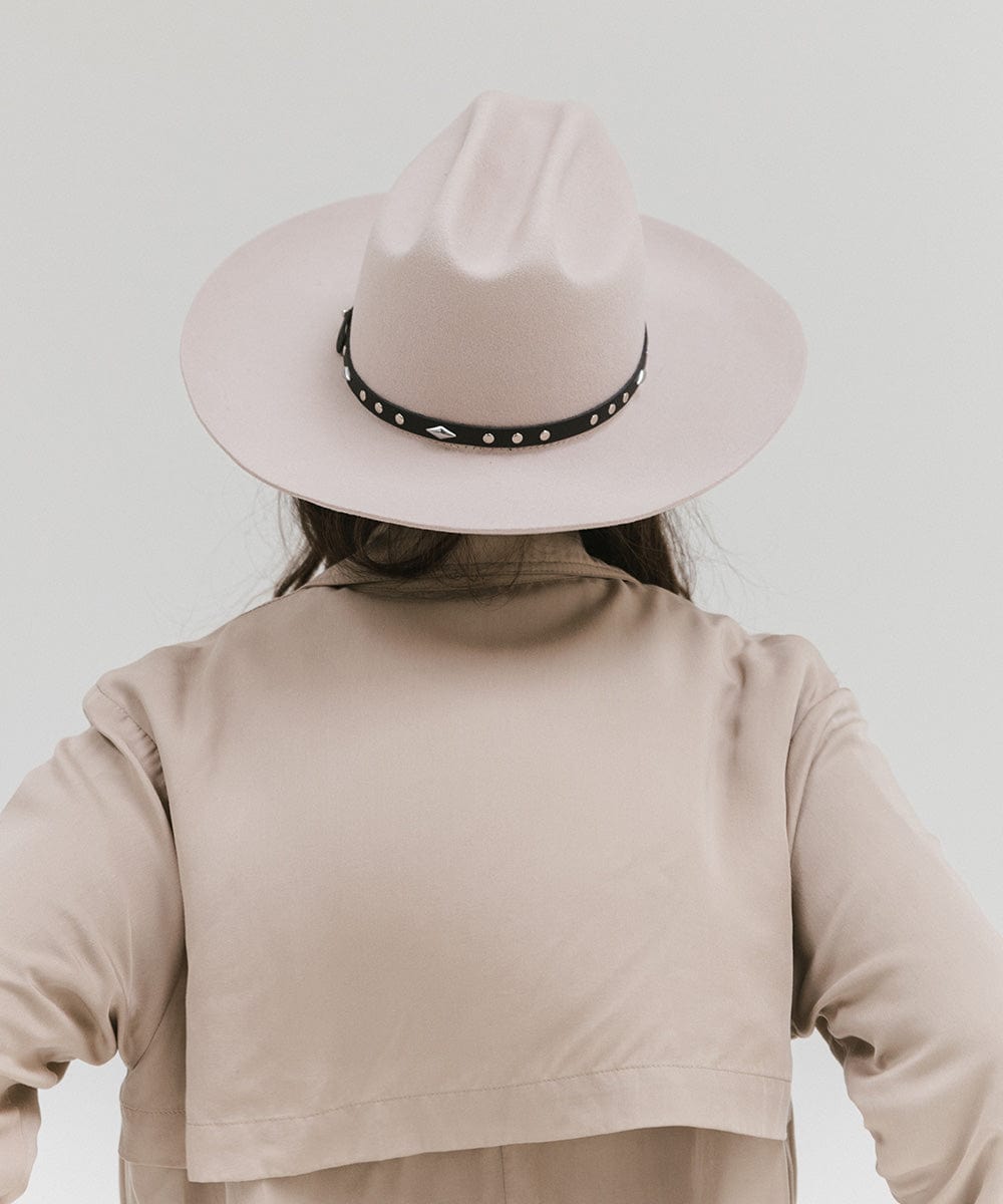Person wearing an ivory colored Western hat with a classic cattleman crown and a black hat band, and a beige coat, facing behind against a plain background #color_ivory