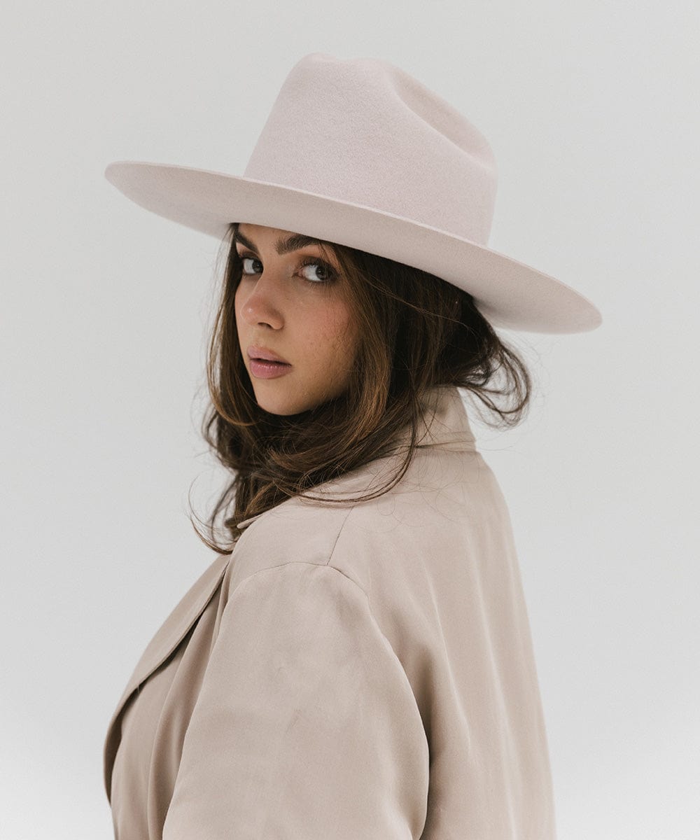 Woman wearing an ivory colored Western hat with a classic cattleman crown, and a beige coat against a plain background #color_ivory